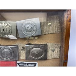Display of eleven German belt buckles including 'SS', Party Buckle, two Army, Fire Service, two Luftwaffe, NSKK, Hitler Youth and WW1 Army; framed with three cloth badges and an armband