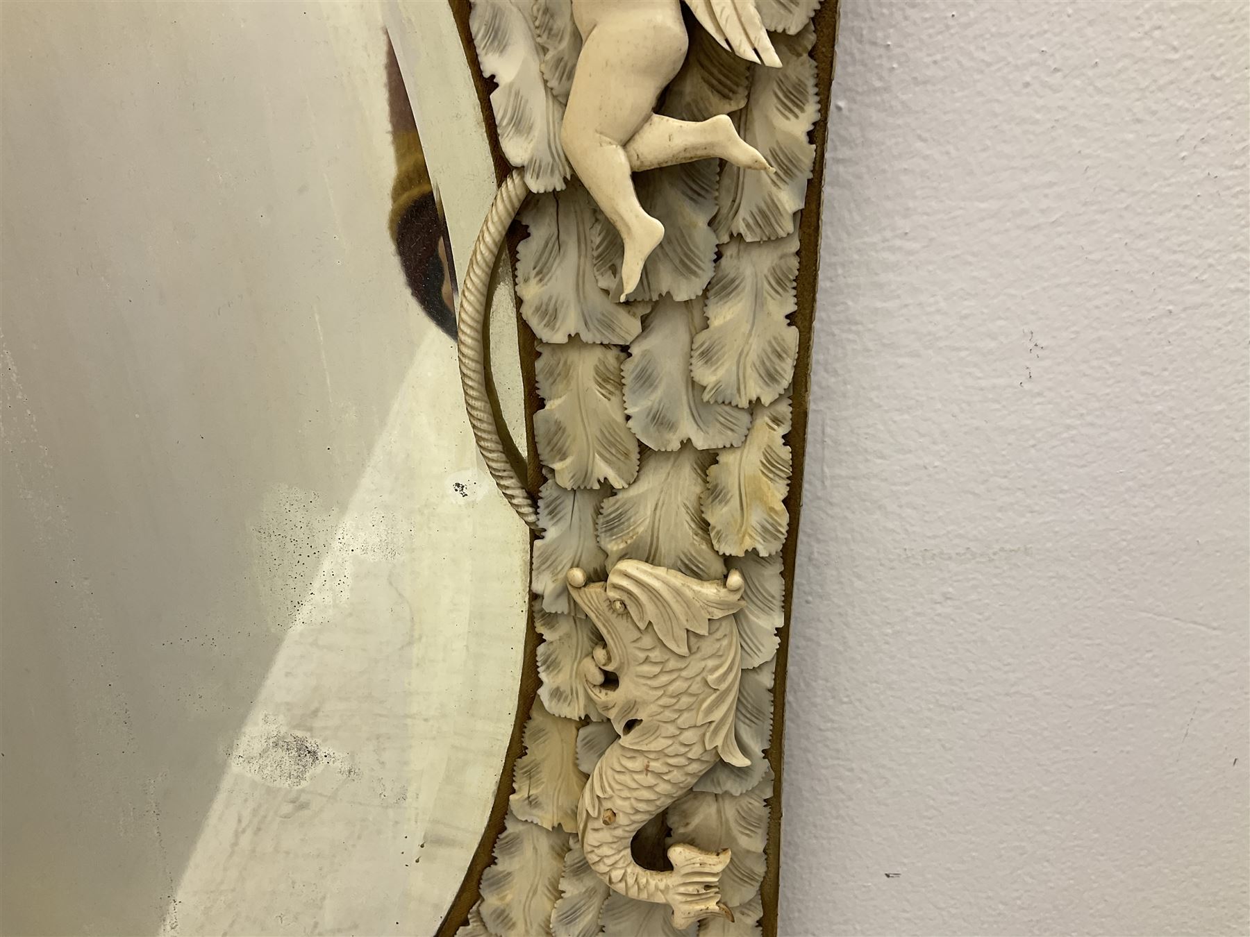 Pair 19th century French Dieppe bone and ivory wall mirrors, the oval bevelled mirror plates within rectangular frames with shaped tops, profusely decorated with ivory leaves, further detailed with carved bone armorial type crest inscribed 'SGOTORVM', putti, fish and mask heads, H81cm W48cm