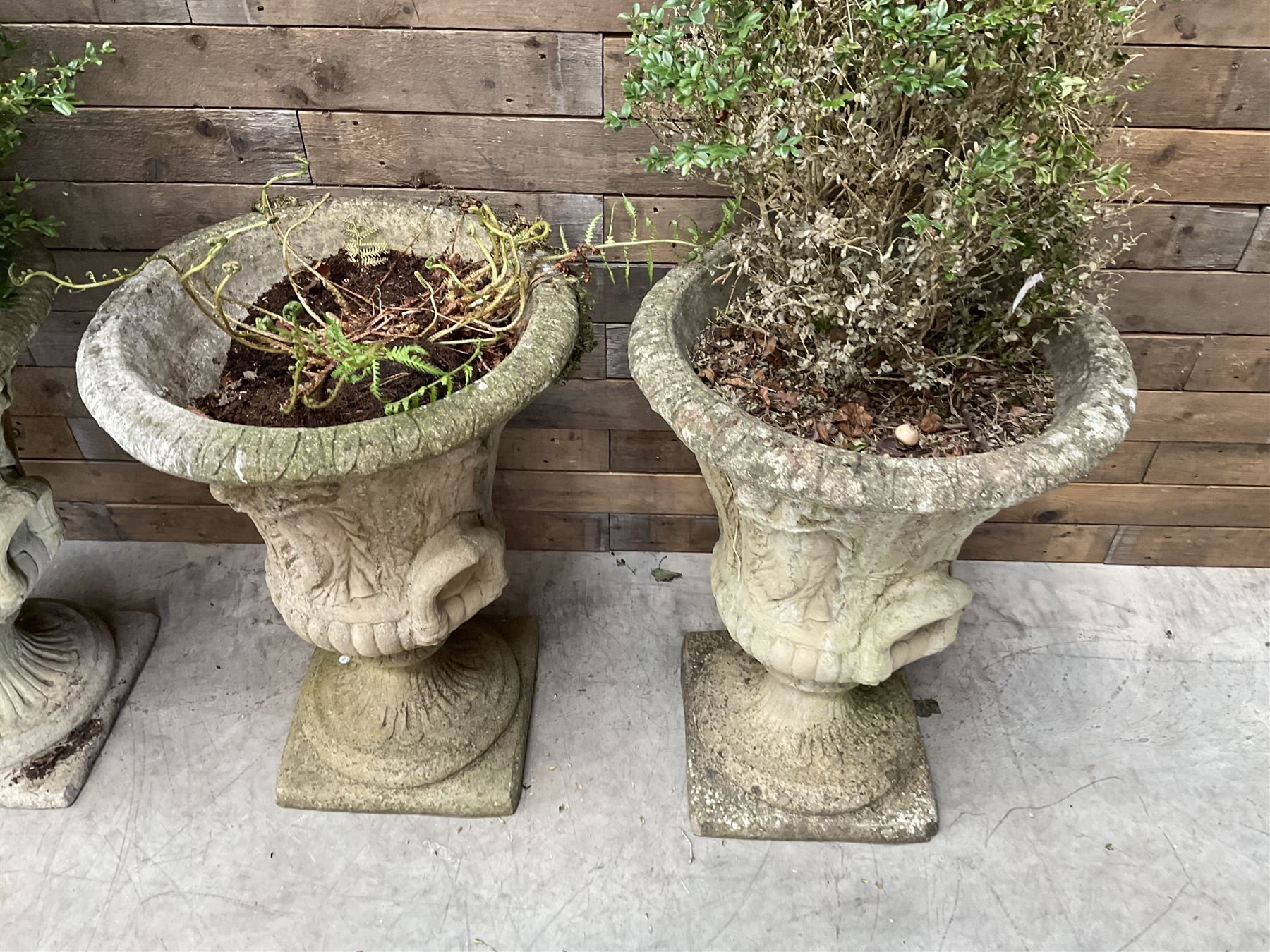 Set of four Victorian design cast stone Grecian urns, tapering form cast with figures and handles, square plinth bases