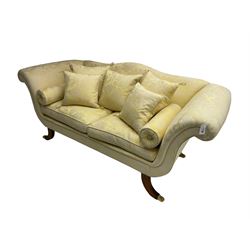 Regency design two seat sofa, serpentine back with scrolled arms, upholstered in pale yellow damask fabric, raised on reeded sabre supports terminating in brass hairy paw feet, with two bolster and five scatter cushions