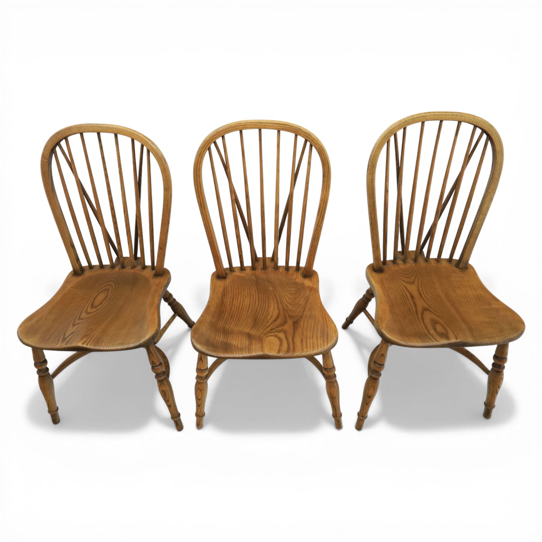 Traditional elm and beech Windsor dining chairs, each with hoop back and turned spindles over a shaped solid seat fitted with loose floral upholstered cushions, raised on turned tapering supports united by crinoline stretchers