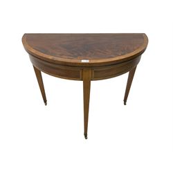 Early 19th century mahogany demi-lune card or side table, inlaid with checkered stringing and satinwood band, the fold-over top with baize lined interior, the frieze rails inlaid with matching design, rear pull-out support with storage well, on square tapering supports with brass castors