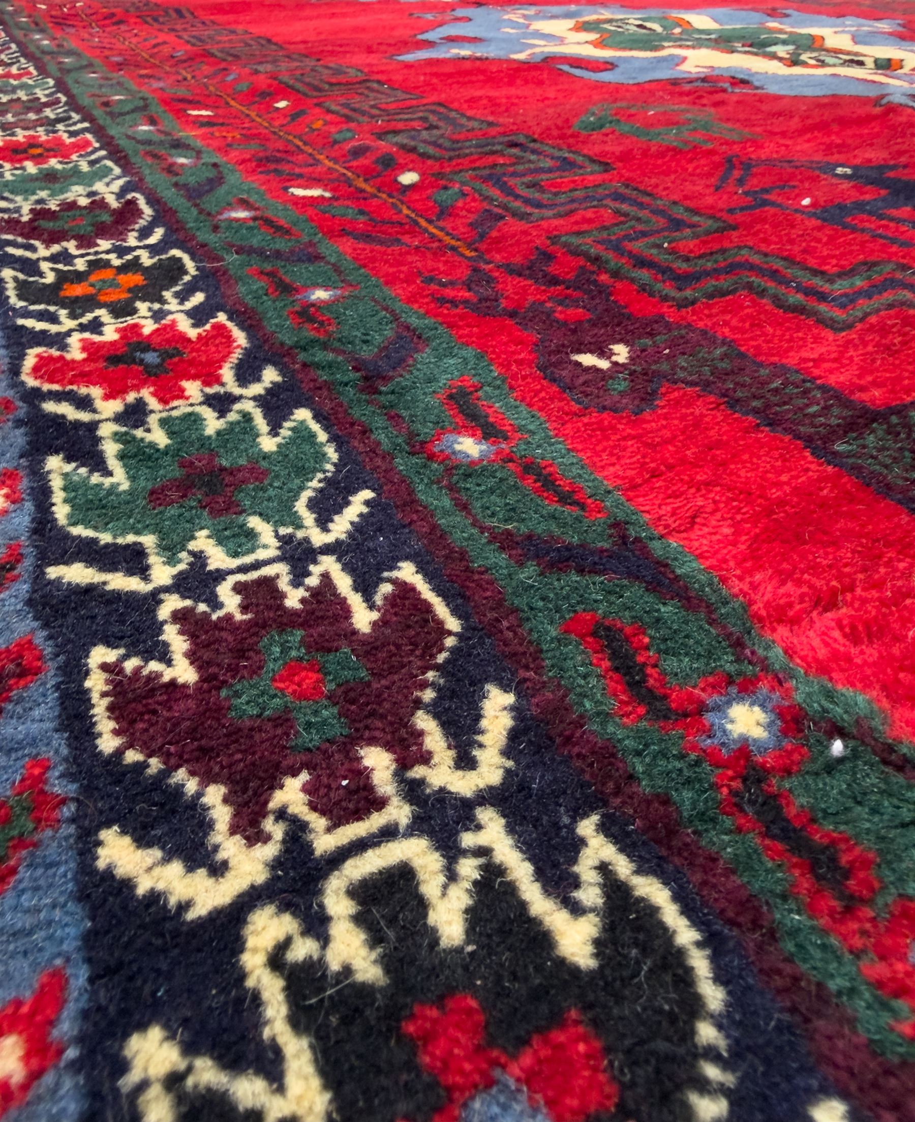 Northwestern Persian Cirjan hand-knotted carpet, madder red field with three linked stepped lozenge medallions in blue, ivory and green, flanked by angular motifs within a dark green border of serrated leaves and rosettes 