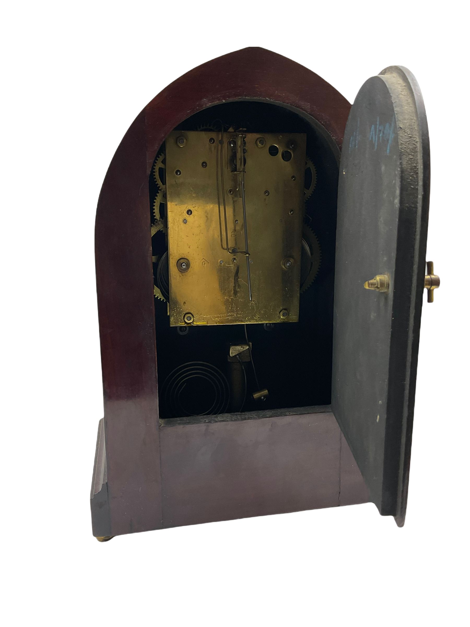 A late 19th century American  mantle clock in a “Lancet” case manufactured by the  Gilbert Clock Factory, Connecticut,  mahogany veneered case with an oval inlay, satinwood stringing to the edge and two recessed brass pillars, on a moulded plinth with four bun feet, enamel dial with upright Arabic numerals and spade hands, fast/slow regulation, with a convex glass and spun brass bezel, eight-day movement striking the hours and half hours on a coiled gong. No pendulum.