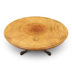 Victorian figured walnut oval loo tilt top table, raised on a heavily carved quatriform base with scrolled supports, terminating in castors