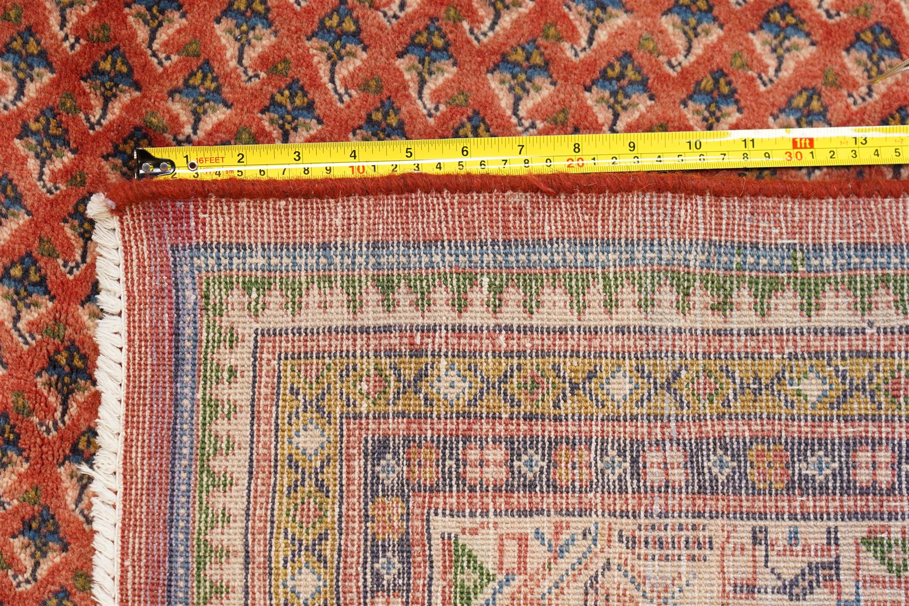 West Persian Boteh-Mir hand-knotted rug, madder red field densely decorated with a repeating lattice of of small boteh motifs arranged in diagonal rows enclosed by a broad border of stylized geometric devices and angular floral ornament between multiple guard stripes with cotton fringe ends