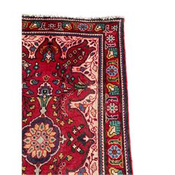 Persian Azerbaijan crimson ground rug, the field decorated with central floral motif and surrounded by trailing floral branches, enclosed within a shaped outer band with further floral decoration, the border with repeating flower heads, geometric guard stripes