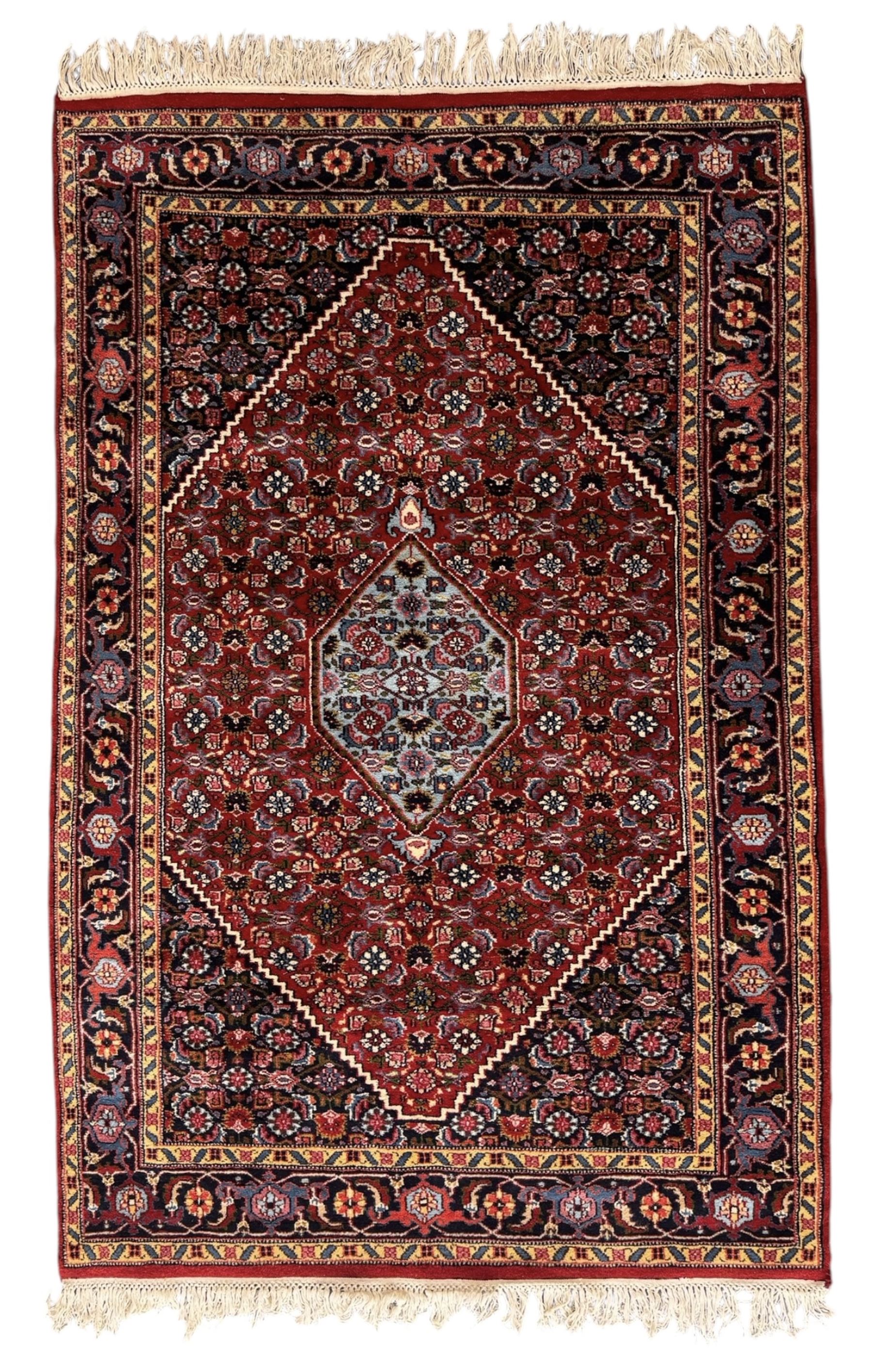 Persian crimson ground rug, central light blue lozenge medallion with floral motifs, the densely decorated crimson field filled with repeating flower heads and trailing leafy vines, the black and red border with interlacing foliate patterns and floral cartouches, surrounded by guard stripes