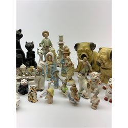 A collection of various ceramic figurines, to include pair of small 19th century Staffordshire cats, Royal Doulton cat, Coalport cat, pair of 19th century pug dogs, two fairings inscribed Good Templars, two Bonzo dog peppers, a number of pin cushion dolls, various 20th century and later black pottery cats, Victorian bisque figures, etc. 