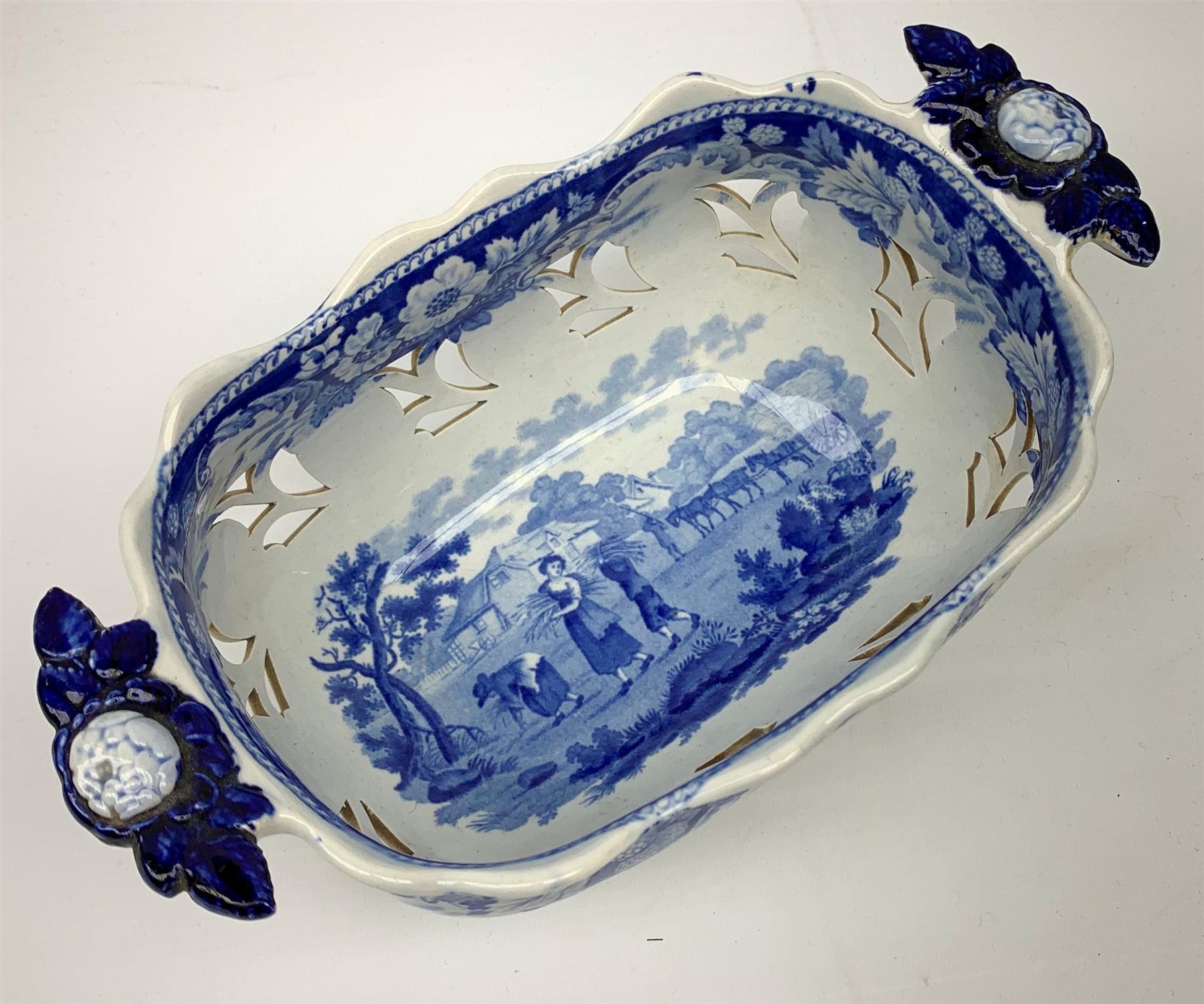 Mid 19th century blue and white transfer printed pearlware reticulated chestnut basket, of oval form with twin handles, decorated to the interior with figures before a classical temple within a garden setting, including handles W26cm, together with a mid 19th century blue and white transfer printed pearlware stand with reticulated edge, decorated with a Willow Pattern, L25cm, and a John and William Ridgeway blue and white transfer printed twin handled pierced basket, decorated with a pastoral scene containing figures at work, with printed mark beneath, including handles L25cm