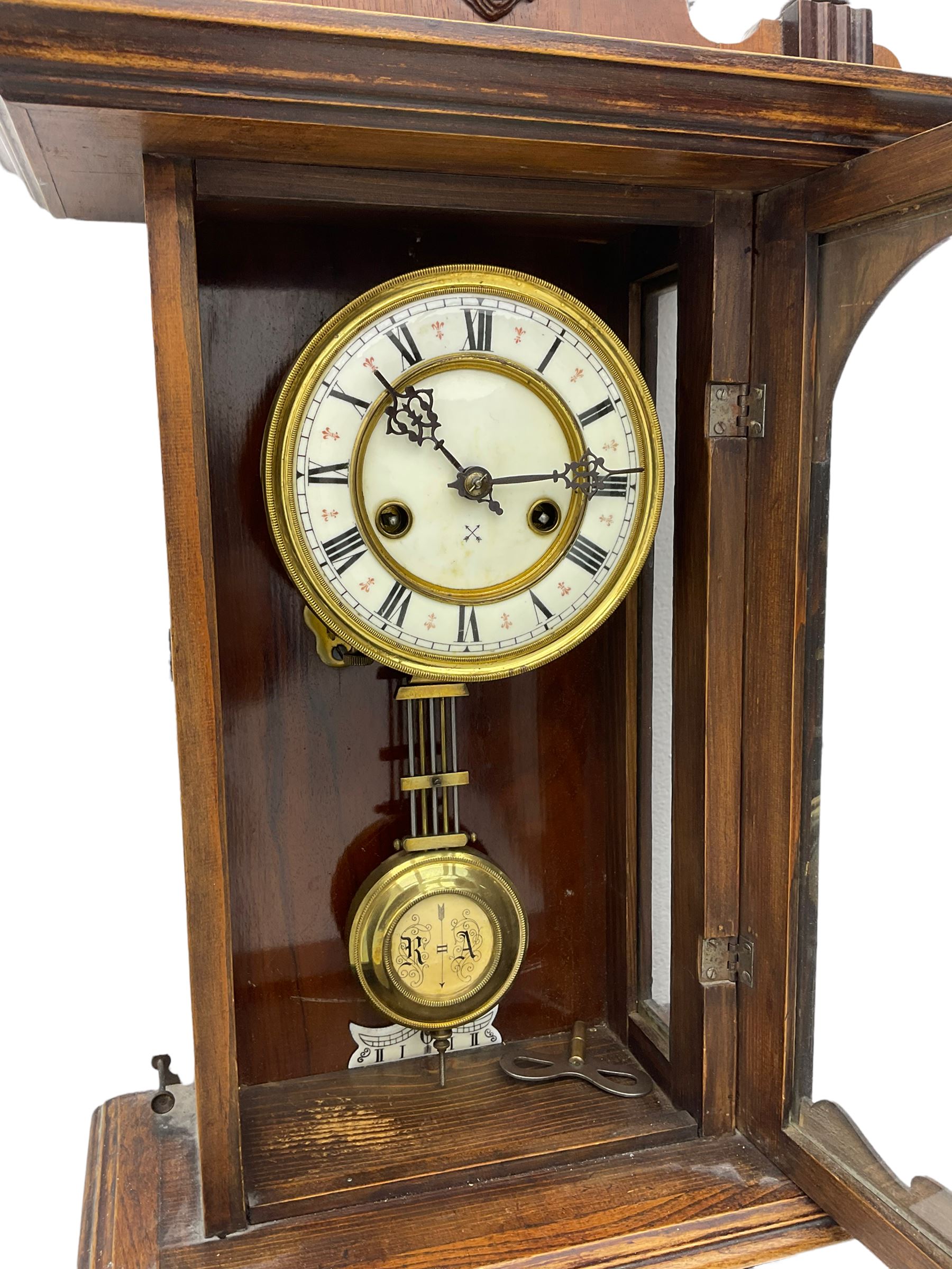 An early 20th century German wall clock with an 8-day HAC spring driven movement striking the hours on a coiled gong, in a mahogany case with a shaped pediment and turned columns flanking a full-length glazed door, with a two-part dial enamel with Roman numerals, minute track and pierced gothic designed hands, gridiron pendulum and beat plate. With Key.





