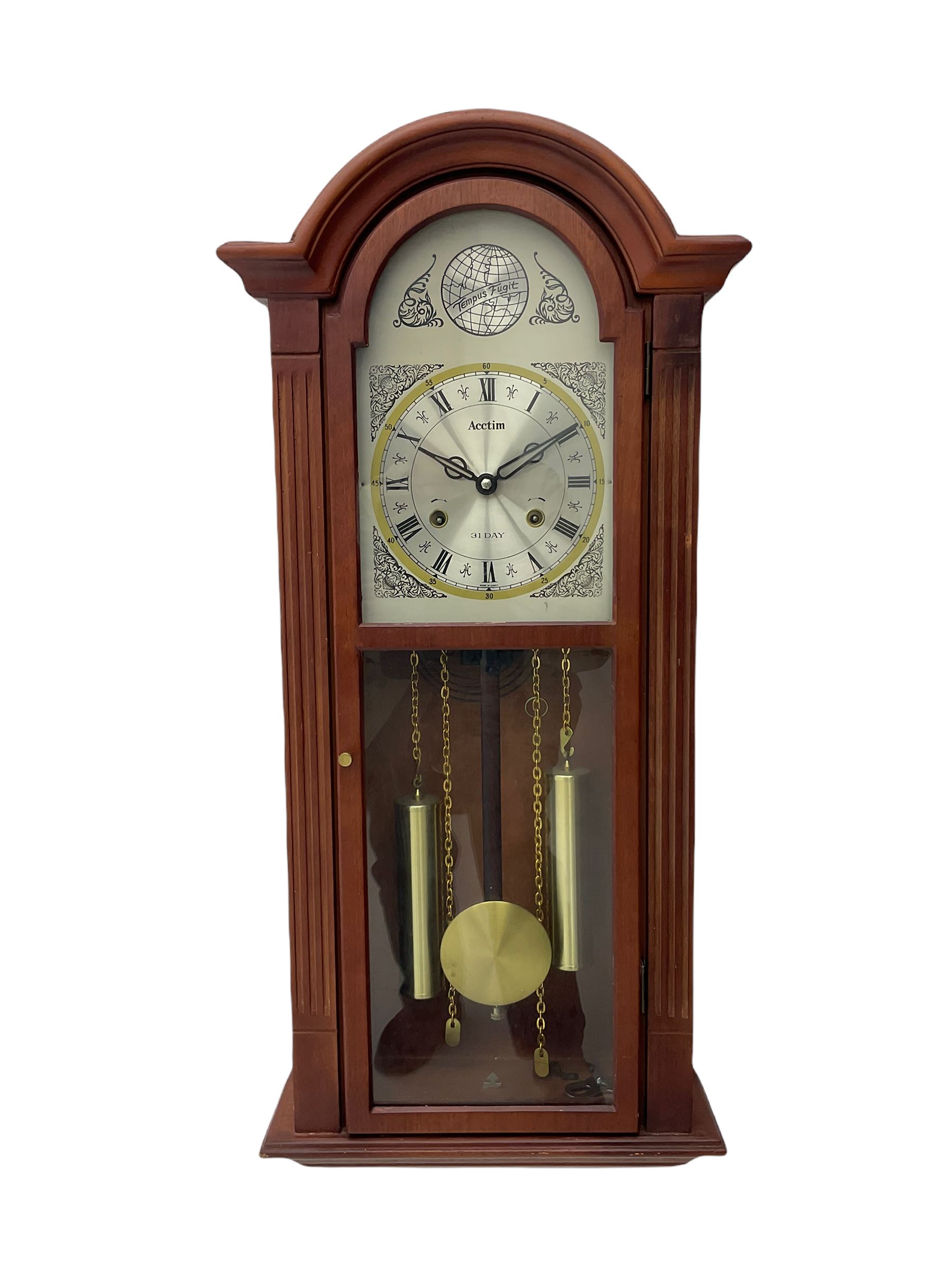 A contemporary Acctim (Anglo continental clock company) thirty-one day striking wall clock in a mahogany effect case with a fully glazed door displaying the pendulum and two dummy wights with chains, with a polished brass dial, Roman numerals, minute track and pierced steel hands, dial plate decorated with spandrels and Tempus Fugit inscribed on the dial brake-arch.
With key and pendulum.

