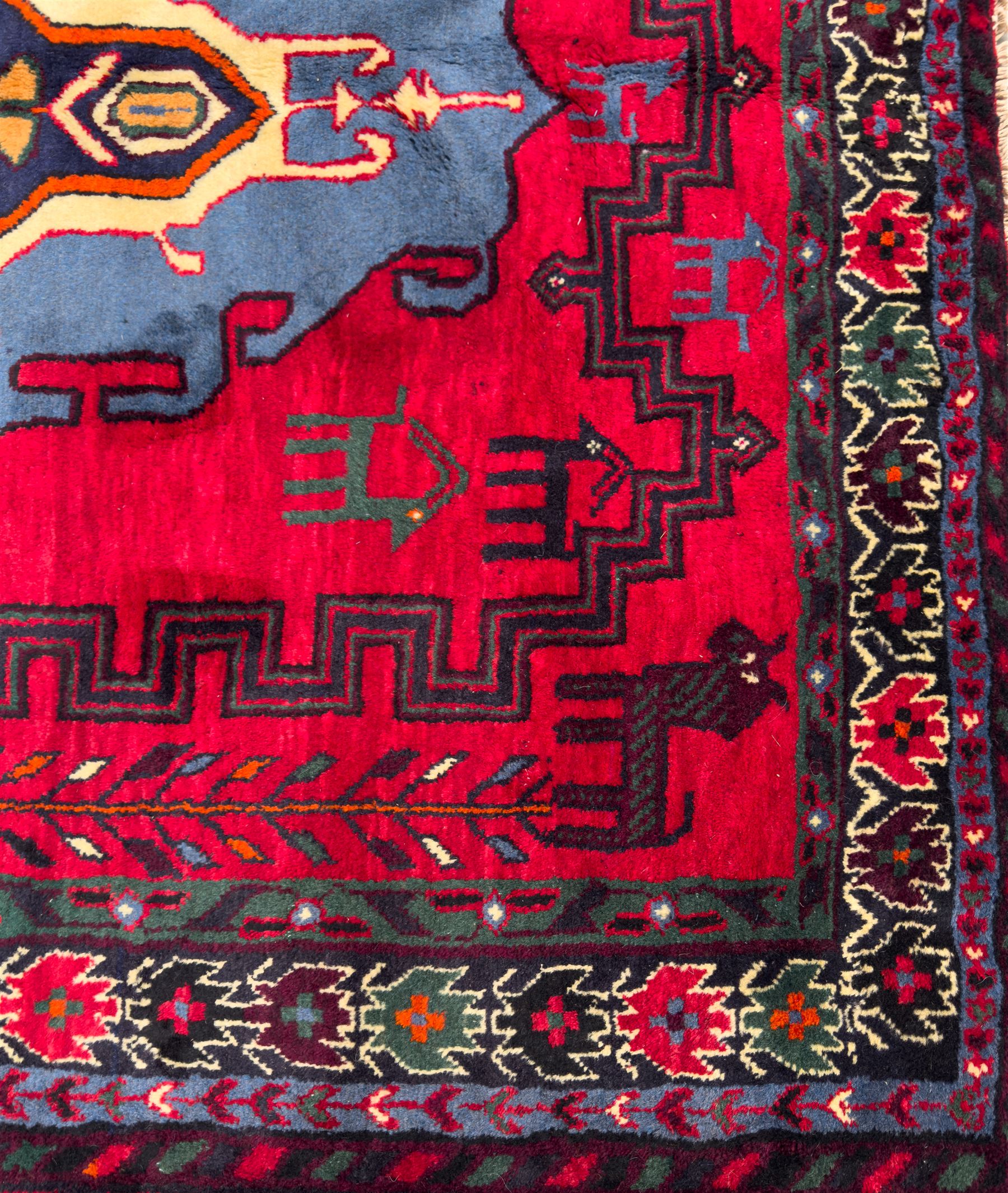 Northwestern Persian Cirjan hand-knotted carpet, madder red field with three linked stepped lozenge medallions in blue, ivory and green, flanked by angular motifs within a dark green border of serrated leaves and rosettes 