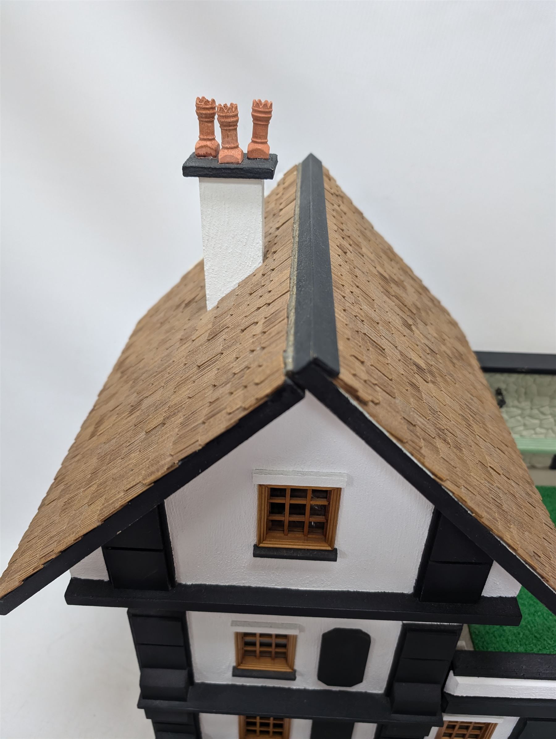 1:24 scale four-storey tudor-style dolls house, with black and white exterior, balcony garden, glazed panelled windows and wooden shingle roof, with decorated interior and wired fireplaces and lighting, H65cm, W58cm, D31cm, 