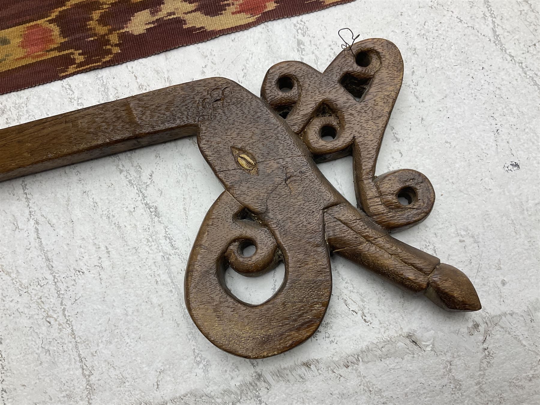 Ikat Man’s Cloth (Hinggi Kombu), East Sumba, Indonesia, woven in red, blue and yellow-brown warp ikat, constructed of two mirroring long panels, the motifs arranged in four bands depicting warrior figures astride rearing horses, high-ranking figures and guardians within geometric borders, on carved wooden wall hanger, L295cm
