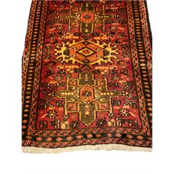 Persian Heriz red ground rug, the field decorated with seven geometric medallions, the field decorated with small stylised motifs of flower heads, repeating three-band border