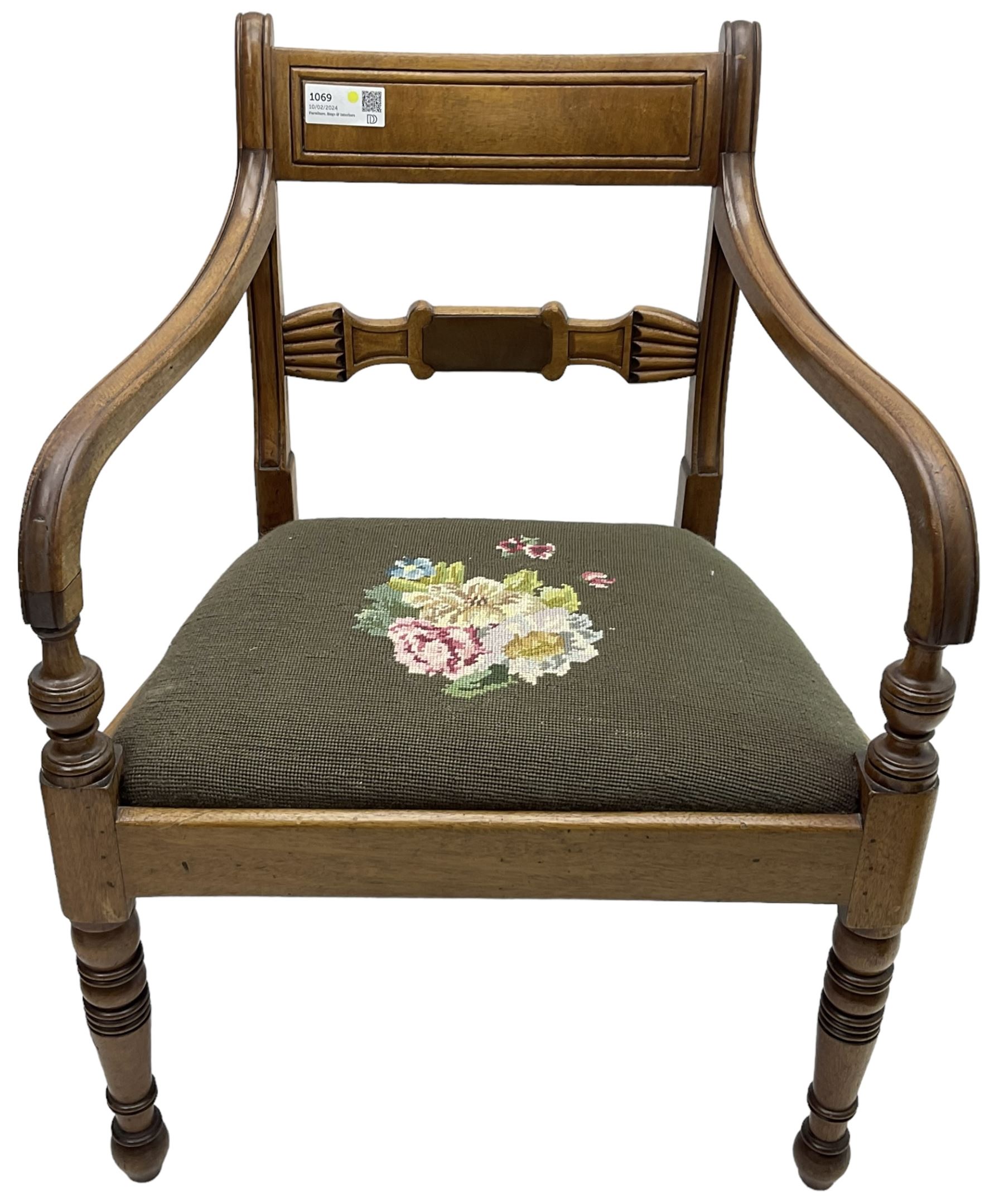 Regency mahogany elbow chair, carved shaped central back bar, over drop-in seat upholstered in floral needlework, raised on ring turned front supports