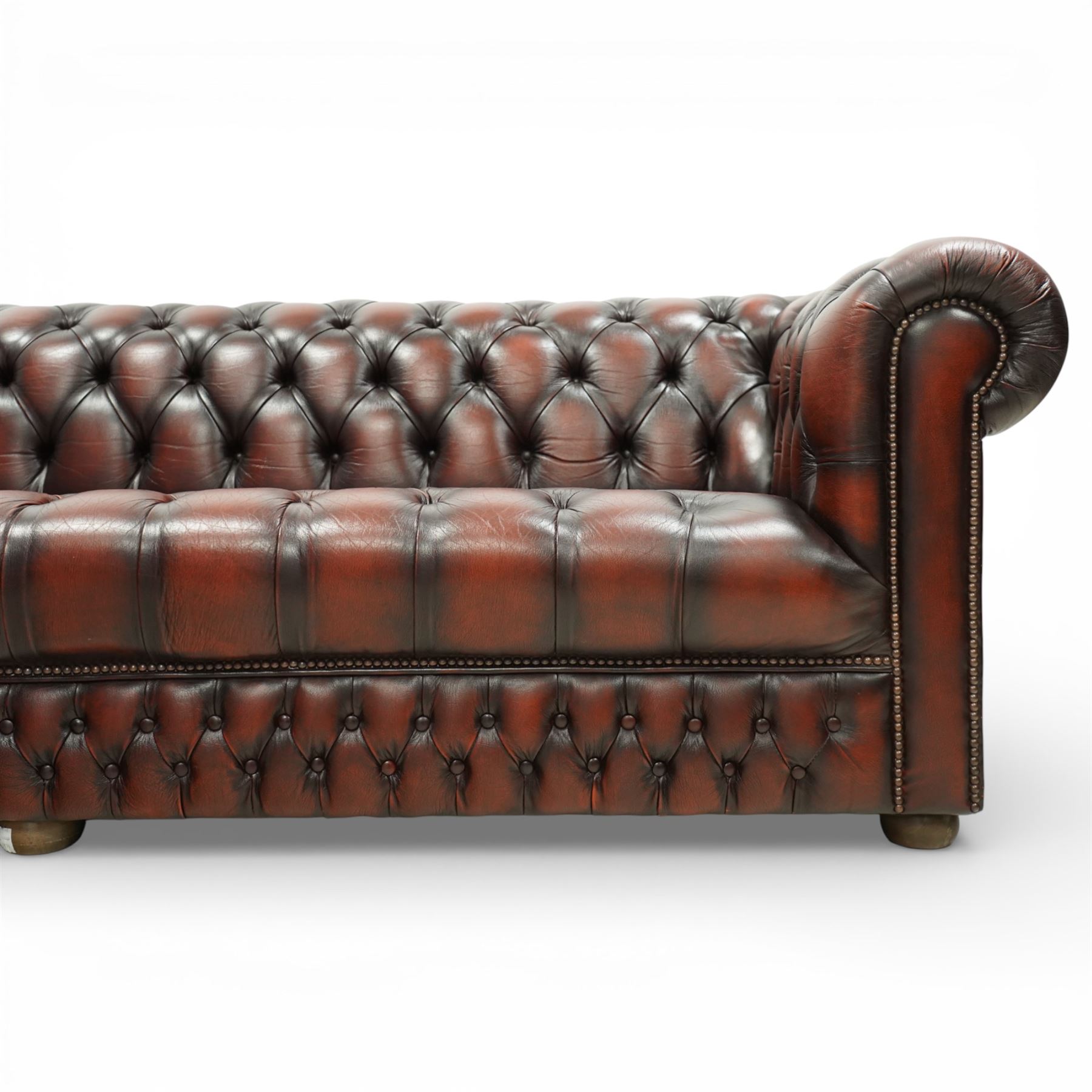 Late 20th century four seat Chesterfield sofa, upholstered in deep buttoned brown leather, with rolled arms, buttoned back and seat, studded detailing and squat feet