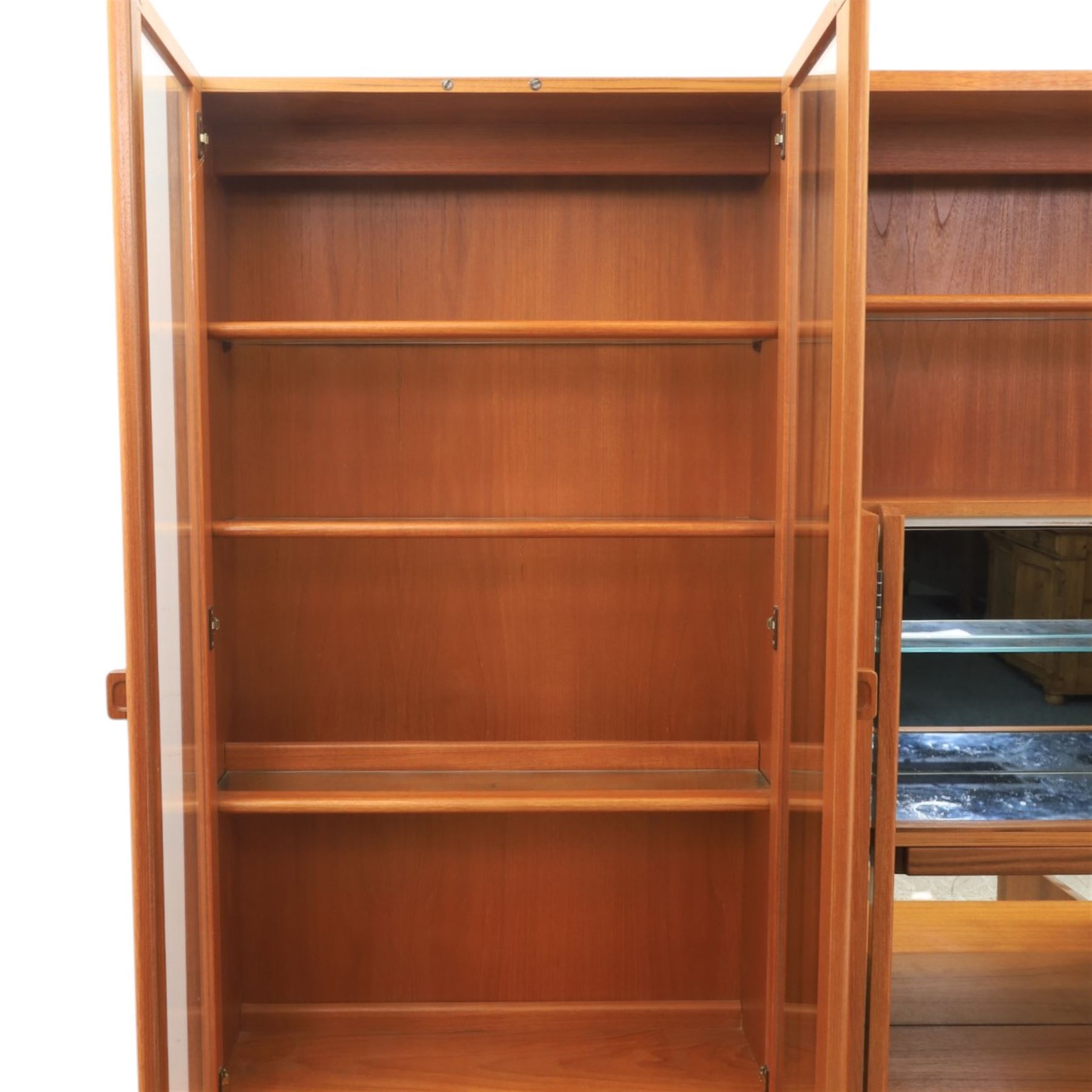 G-Plan - Mid 20th century teak modular wall unit, the upper section fitted with twin glazed doors enclosing shelves, adjoining concertina doors with mirrored and shelved interior, the base with four cupboard doors with recessed rectangular handles, raised on a plinth base