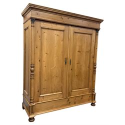 Large 19th-century Continental polished pine double wardrobe, panelled back and doors revealing brass hanging rod, flanked by half-turned columns with Corinthian capitals supported on bun feet