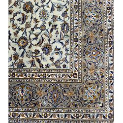 Central Persian Kashan hand-knotted carpet, the ivory ground intricately decorated with scrolling vines, palmettes, and stylised flowerheads in soft blue, gold and brown tones, enclosed by a broad indigo border with repeating floral motifs and multiple guard stripes