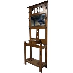 Arts & Crafts period oak hall stand, projecting moulded cornice over arched cut-out decorated with shaped vertical rails, fitted with rectangular bevelled mirror back over hinged glove compartment, on straight pierced supports with shaped pediments 