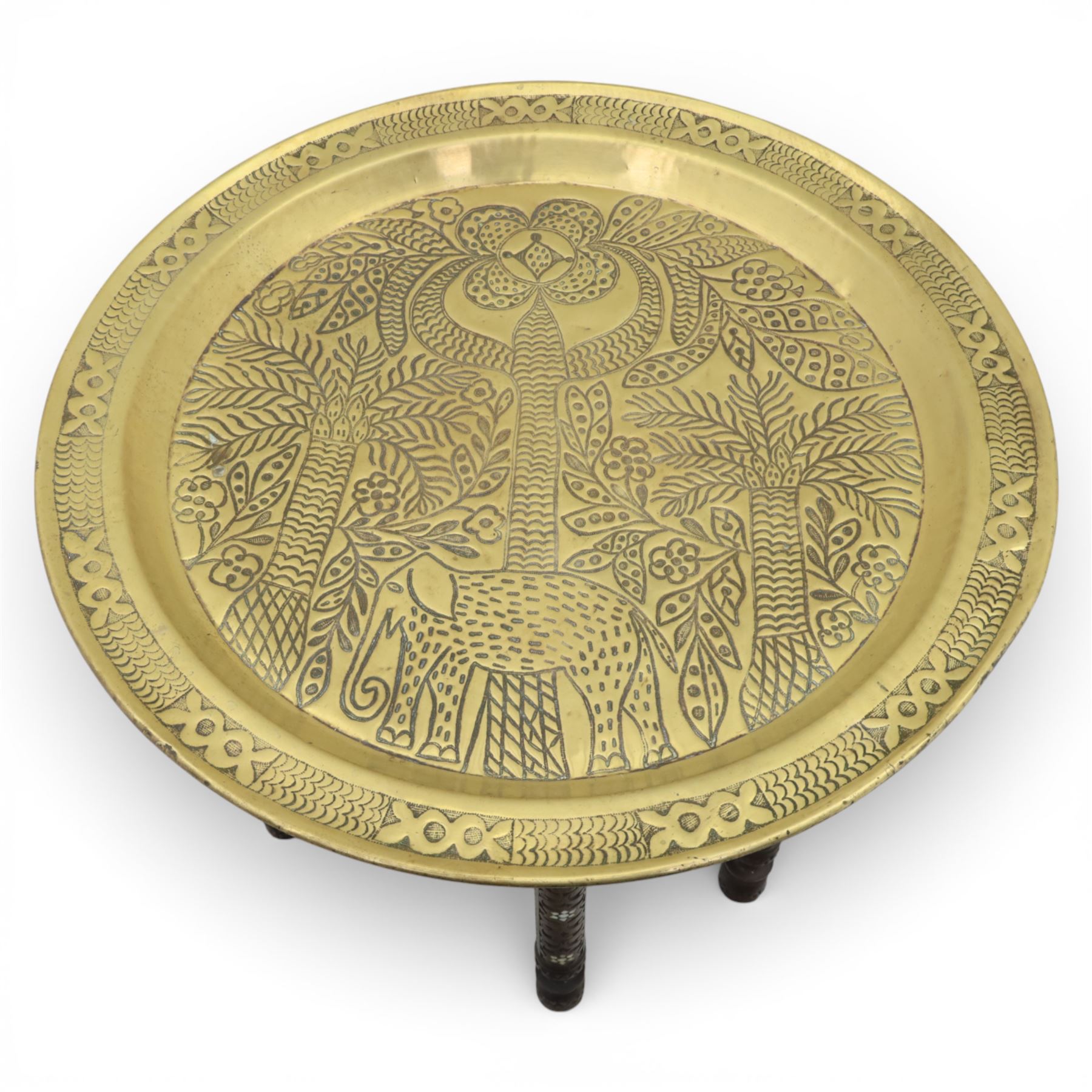 20th century Eastern brass charger topped table, the circular brass trap chased with an elephant, palm tress and flowering vines, supported upon a folding stand with six turned legs with inlaid detail, united by turned supports