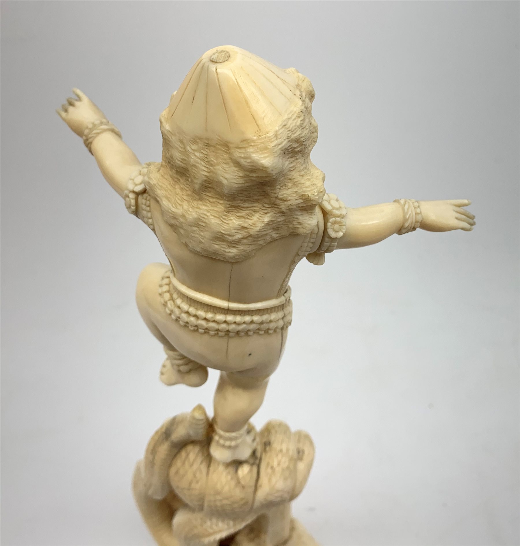 A large Japanese carved ivory okimono, modelled as a figure stood upon one leg with arms outstretched, upon a five headed serpent emerging from waves, H30cm.