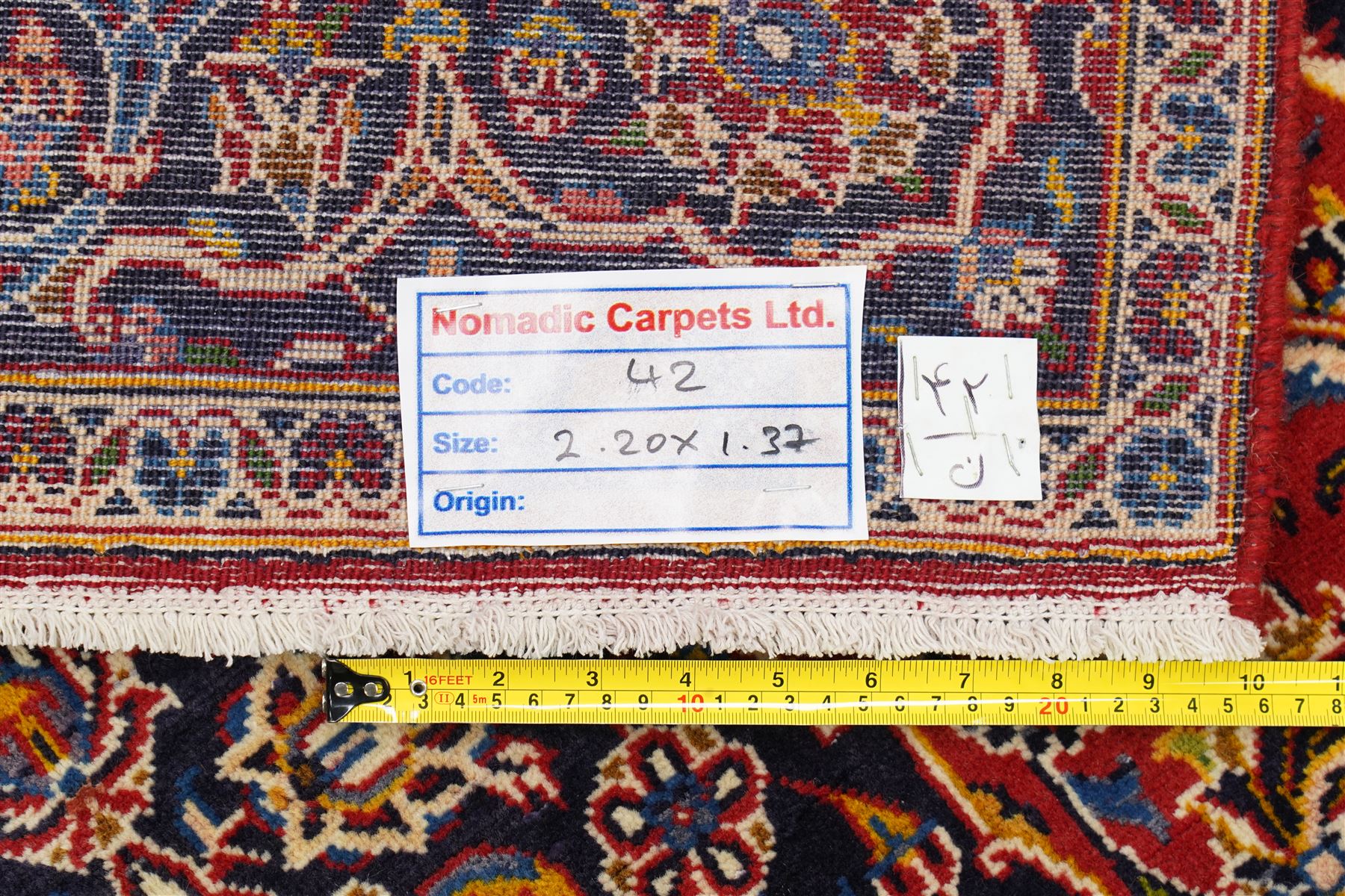 Central Persian Kashan hand-knotted rug, madder red field, with central lobed medallion with pendants, issuing an all-over design of scrolling vine, palmettes, and floral sprays, with conforming spandrels, enclosed by a broad indigo palmette and vine border framed by guard stripes in a palette of navy, blue and ivory tones, with cotton fringe ends 