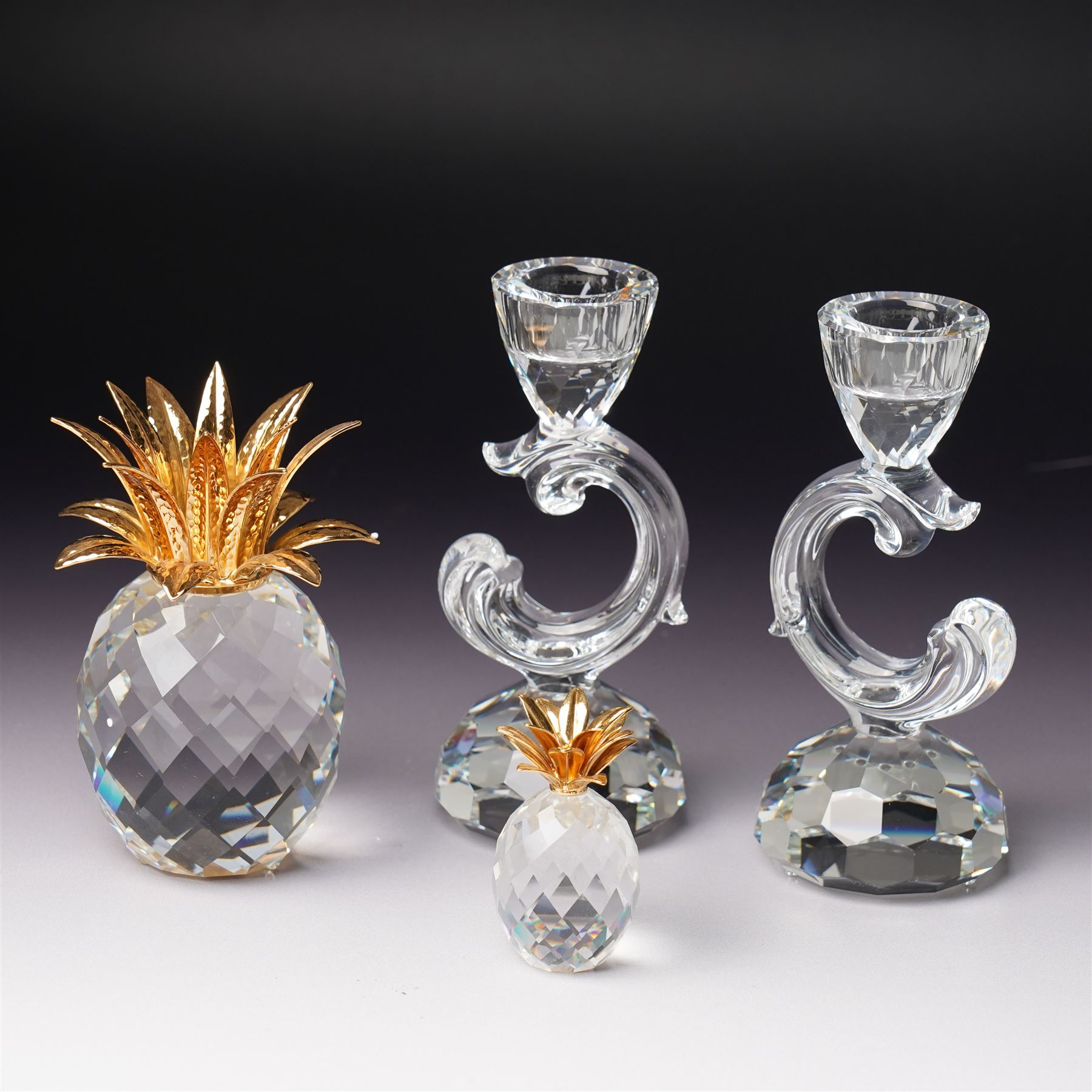 Pair of Swarovski Crystal candlesticks, boxed, together with two paperweights in the form of pineapples with gilt mounts, a large and small example, boxed (4)