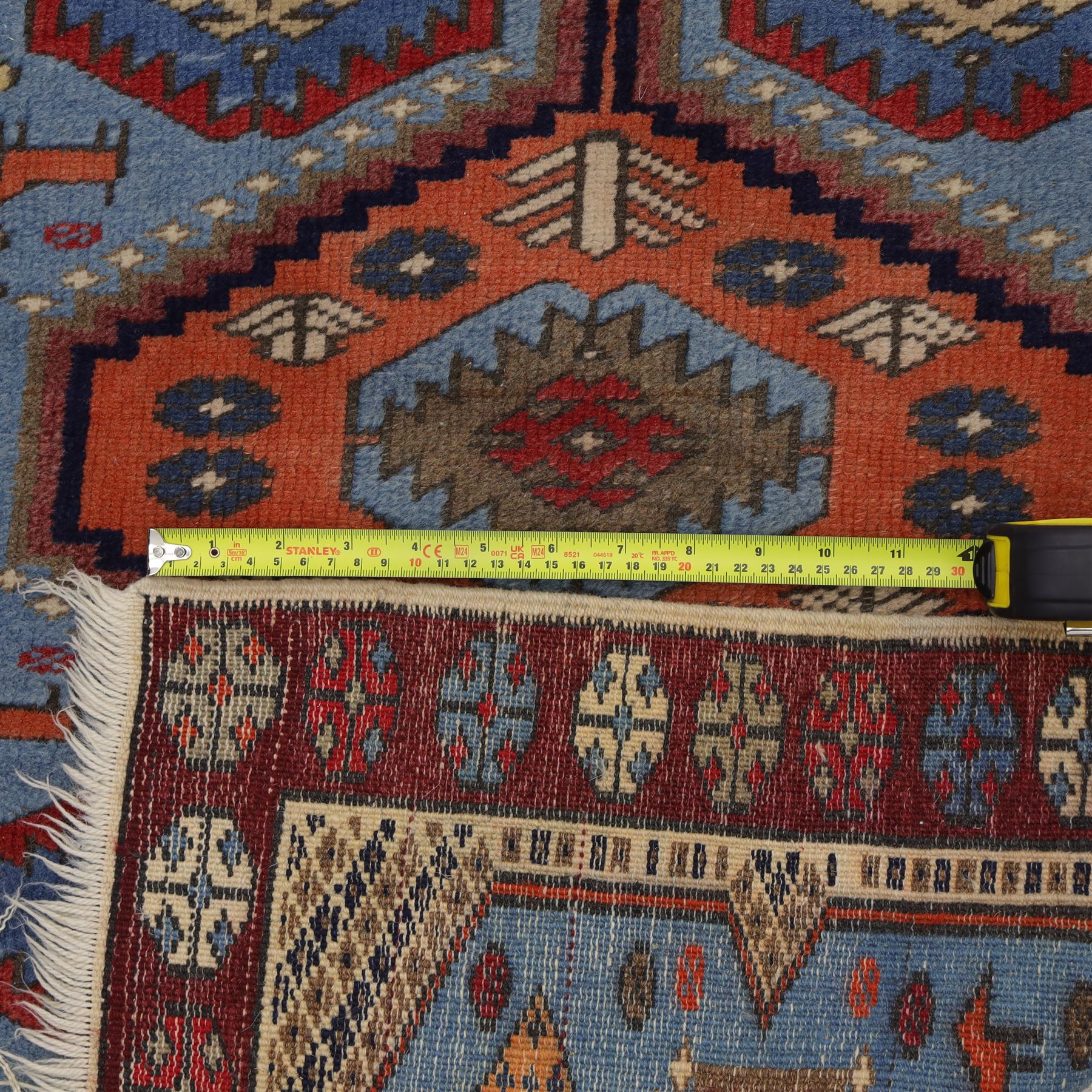 Caucasian Kazak hand-knotted rug, pale blue main field with large geometric medallions in a vertical arrangement and angular tribal motifs within a rosette and geometric border, cotton fringe end, 68x88cm