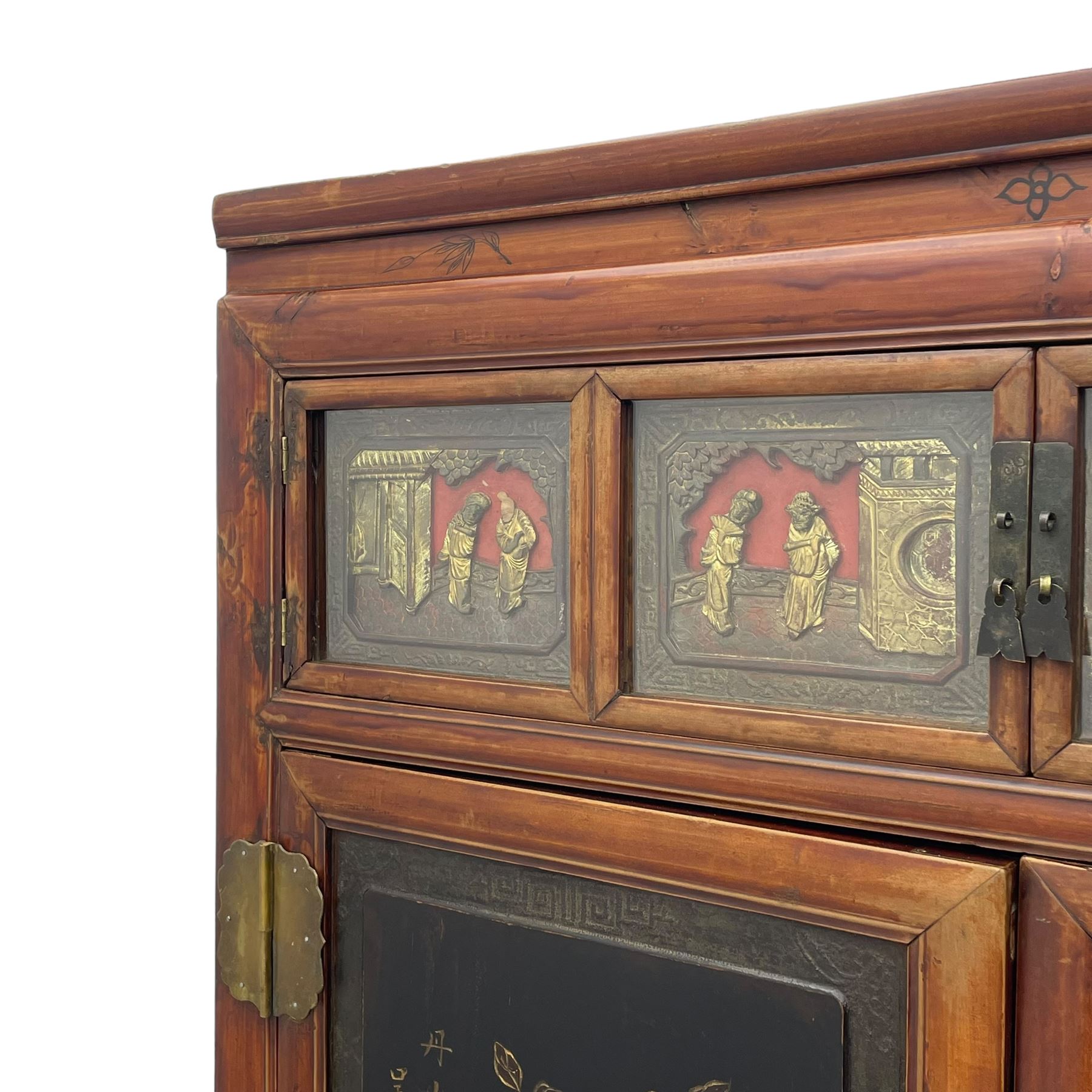 Late 19th century Chinese Qing dynasty red and black lacquered wood cabinet,  Fujianese province, upper cupboard enclosed by two doors with relief carved and gilt panels depicting figures behind glass, the large cupboard enclosed by two panelled doors carved with trailing foliate branches and birds, inscribed with Chinese characters, to the left ‘The red mountains are in the shape of Phoenixes and appear auspicious’ and to the right, ‘Wealth and honour are given by flowers and I hear the sound of the phoenix', fitted with two drawers, on square supports with carved brackets 