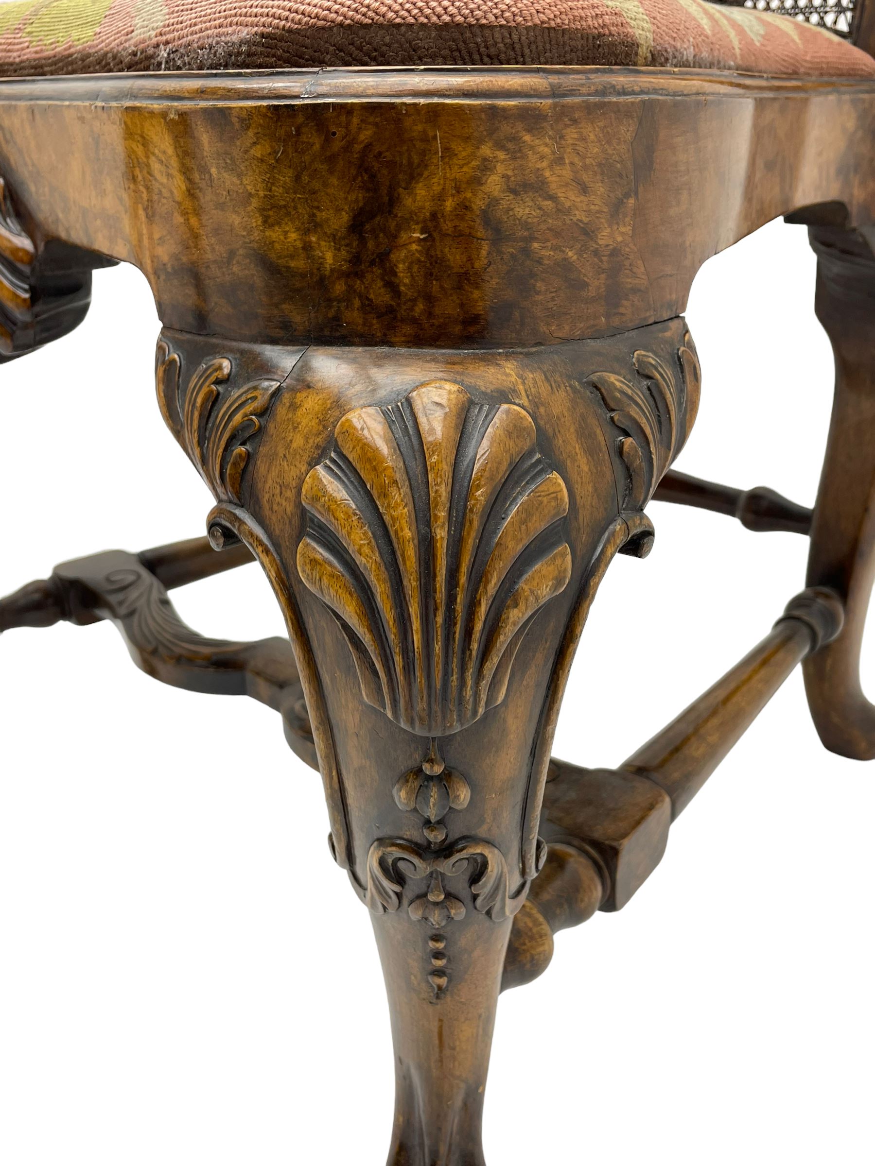 Pair of early 20th century Queen Anne design chairs, the cresting rail carved with scroll and central shell motif, shaped uprights and splat encased in cane work panels, shaped moulded seat frame with shell motif, floral needlework upholstered drop-in seat cushion, on shell carved cabriole supports with ball and claw feet, united by turned and shaped middle stretcher carved with acanthus leaf