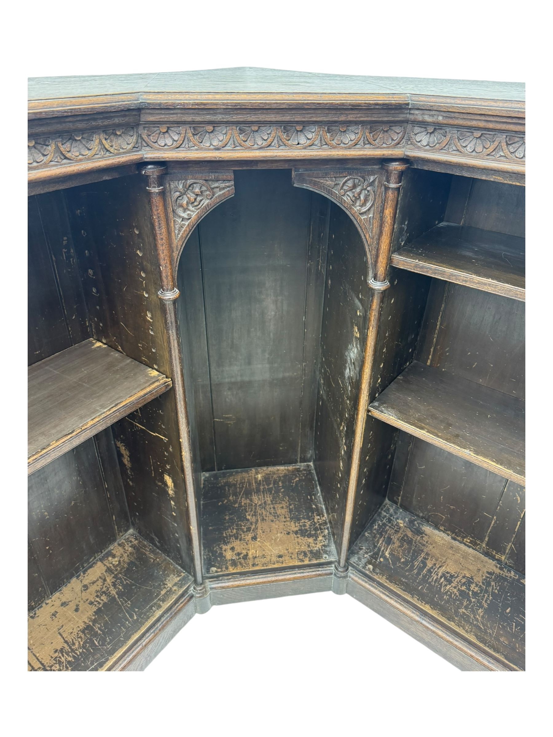 Victorian carved oak corner bookcase, L-shaped form, moulded top over lunette carved frieze, decorated with S-scroll and mask carved corbels with trailing acanthus leaves, fitted with adjustable shelves, on moulded plinth base 