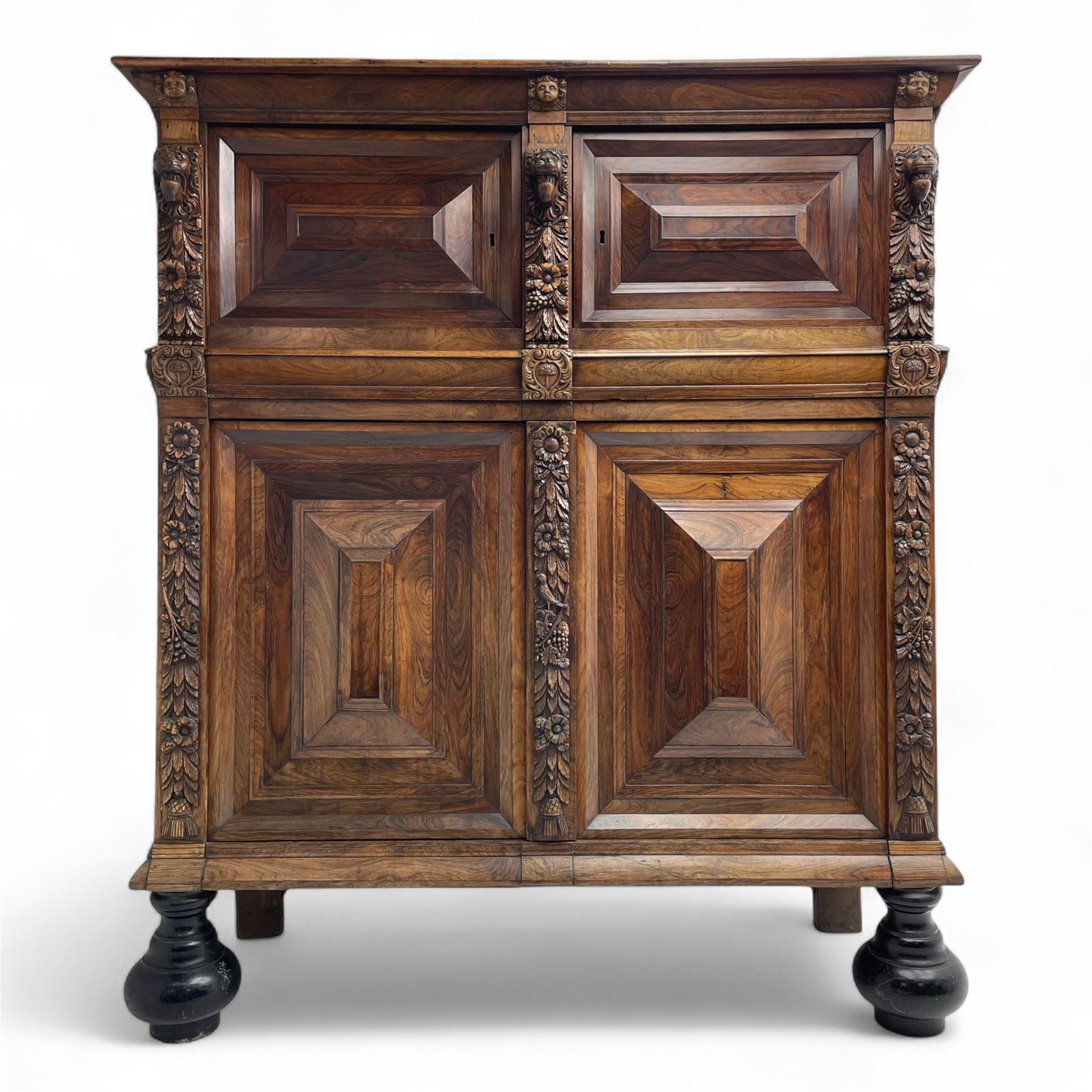 Late 17th century Flemish/Dutch rosewood and oak ‘Zeeuwse Kast’ or cupboard, projecting cornice carved with three putti masks, the uprights carved with lion masks over ribbons, flower heads and foliage, enclosed by four geometric panelled doors, lower central upright carved with flower head over foliate ribbon with bird among foliage, the escutcheon hidden by swivel berry carved cover, interior fitted with shelves, two drawers and shallow hinged cupboard, on two large turned and ebonised feet, circa 1680