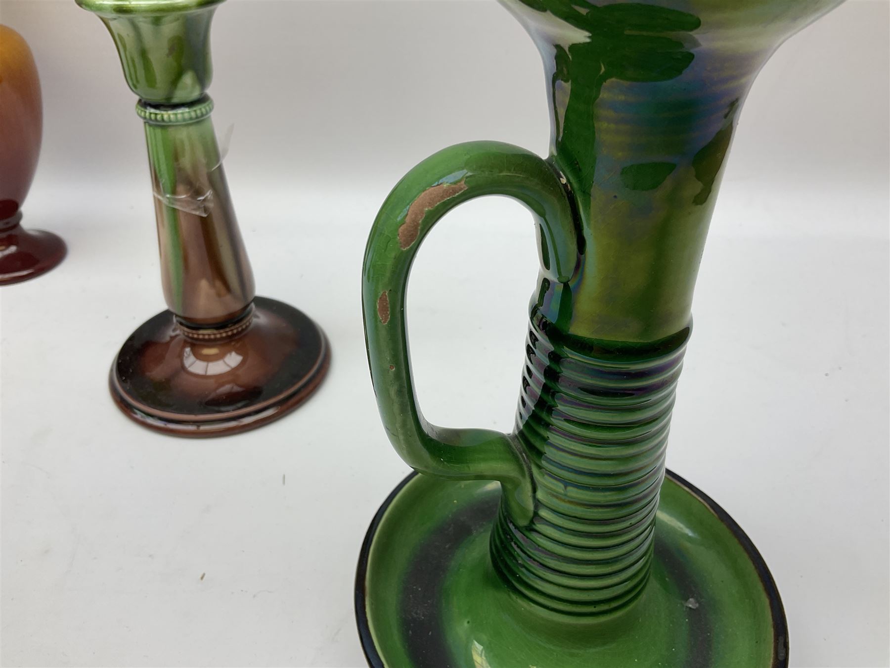 Linthorpe pottery vase with crimped rim and ovoid body, Linthorpe jug with high loop handle and crimped spout, a pair of candlesticks with a green, brown glaze and other similar pottery 