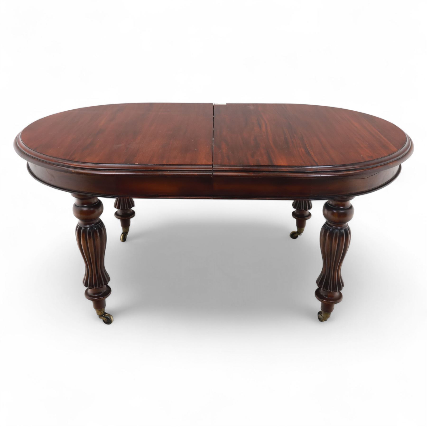 Victorian mahogany extending dining table, rounded rectangular top with moulded edge, pull-out action fitted with two additional leaves, raised on four reeded and fluted baluster legs with brass caps and castors