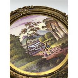 19th century painted porcelain plaque, of circular form, depicting a landscape with hilltop castle in the background, river, and figures and ruin to the fore, in gilt frame, plaque D22cm overall D27.5cm