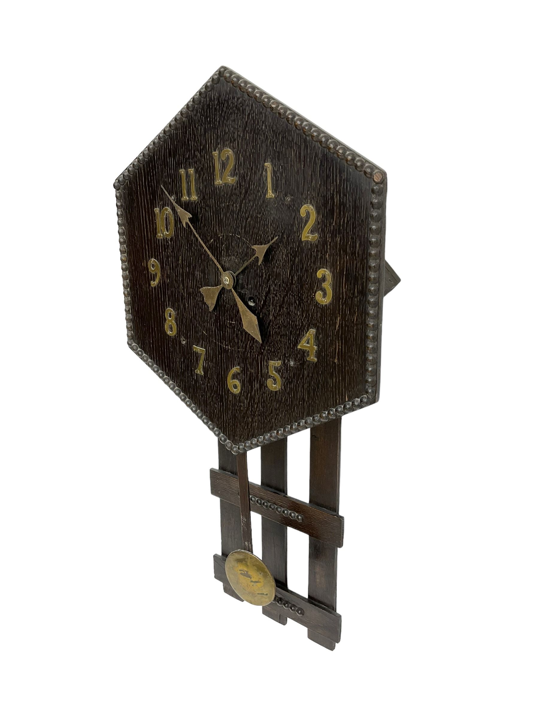 1920’s Art deco drop dial wall clock - with an eight day spring driven timepiece movement, hexagon dial in dark oak with applied brass Arabic numerals and arrow shaped hands, open framework backboard, visible wooden pendulum with a brass faced bob.