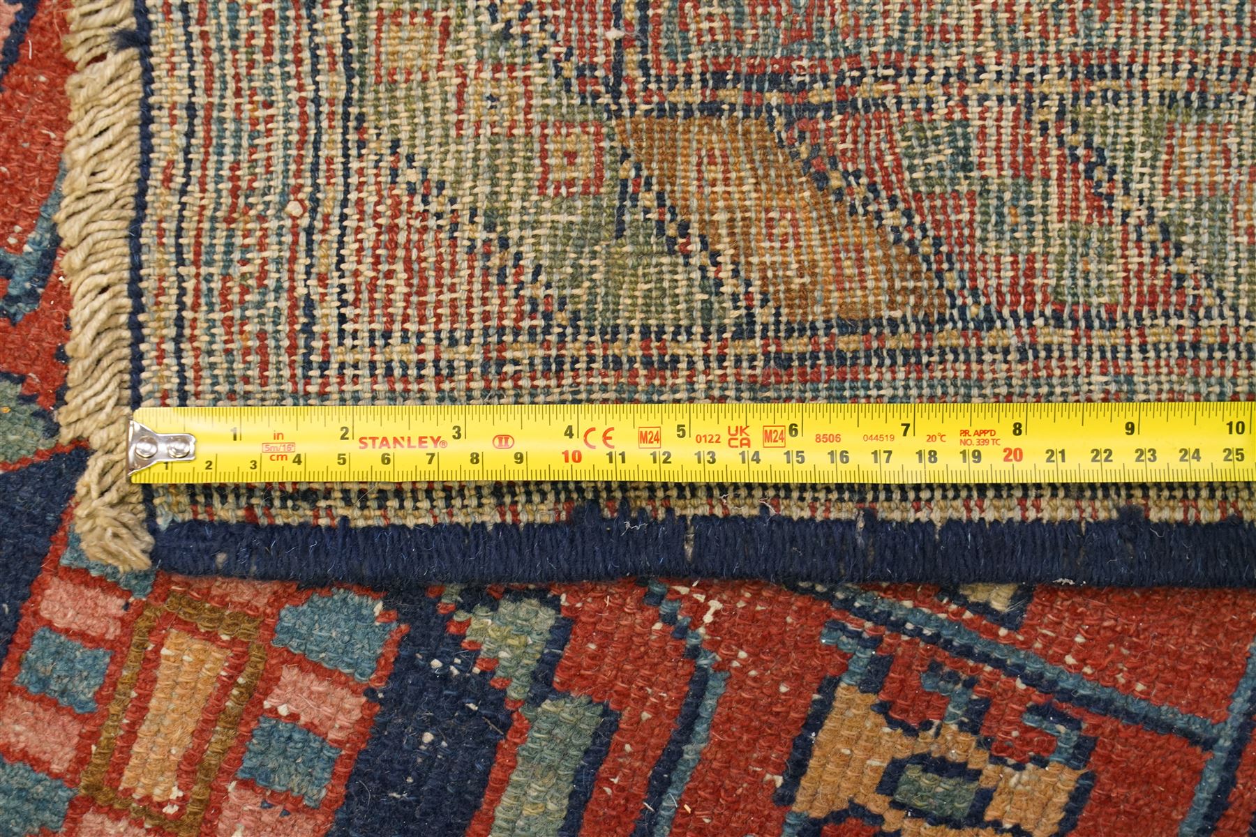Persian Heriz hand-knotted carpet, terracotta ground centred by large dark navy geometric medallion with stepped outline, decorated throughout with stylised flowerheads, palmettes and geometric motifs in blue, green and ochre, enclosed by diagonal geometric border with narrow guard stripes