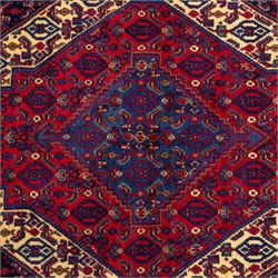 North West Persian Senneh hand-knotted rug, dark indigo field with a central bold stepped lozenge medallion of madder red and deep blue, enclosed within an ivory serrated contour forming a cruciform outline, medallion with repeating boteh and floral devices, field decorated with an all-over Herati pattern of rosettes enclosed by angular leaves principal border of madder red ground decorated with alternating floral heads, flanked by narrow guard stripes, with cotton fringe ends 