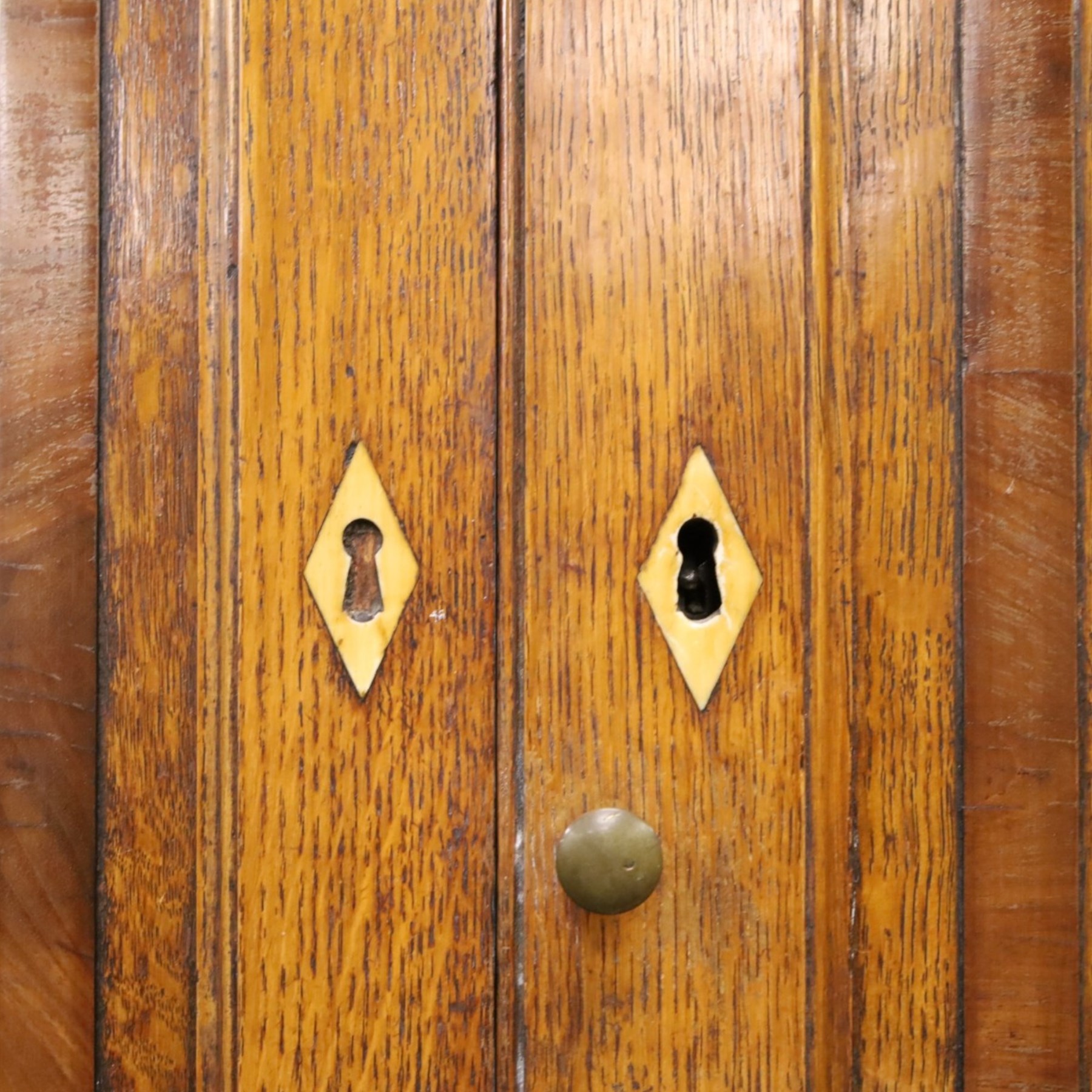 Georgian oak and mahogany housekeepers cupboard, the upper section with projecting cornice, crossbanded and inlaid frieze, above panelled doors with bone escutcheons, enclosing three fixed shelves, flanked by barley twist quarter pilasters, the lower section with further crossbanded and inlaid frieze, two short over two long graduating drawers with ebonised handles, raised on turned supports 