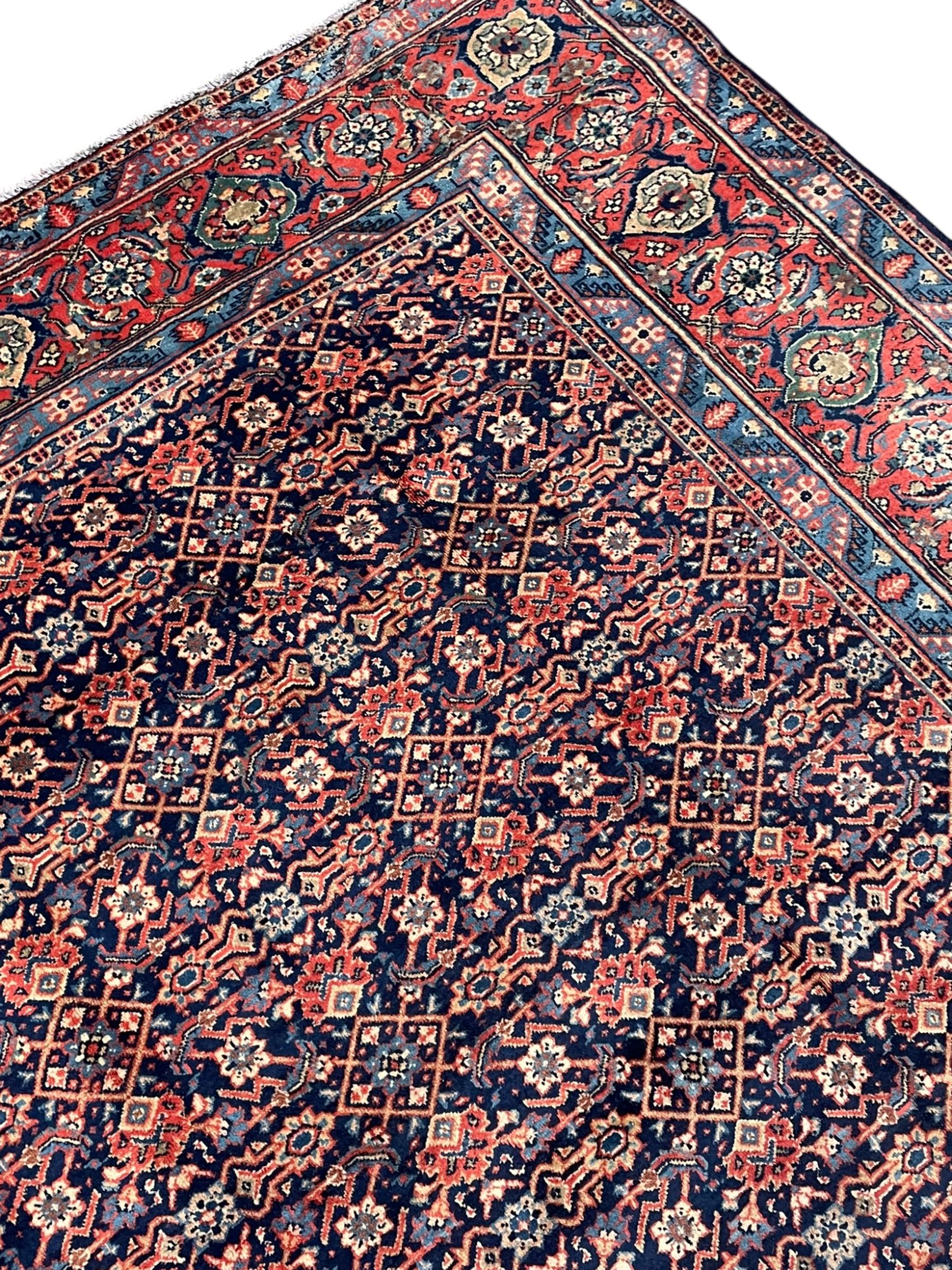 Persian Heratti indigo ground carpet, the busy field decorated with repeating floral pattern Heratti motifs, scrolling leafy branches and palmettes to the crimson ground border, within foliate pattern guard stripes 