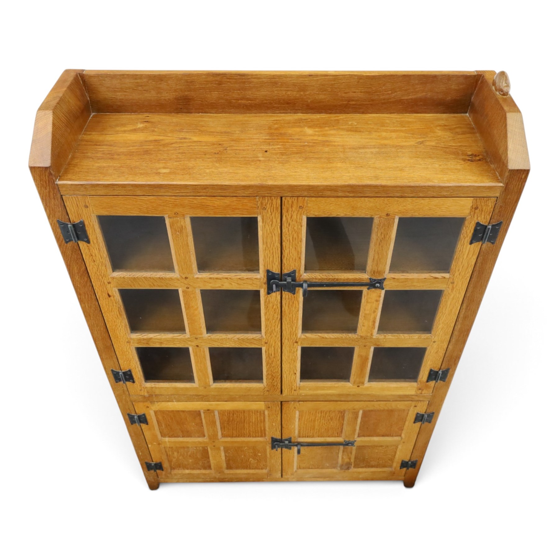 Rabbitman - oak glazed bookcase or display cabinet, lightly adzed rectangular top with raised gallery, twin glazed doors enclosing two shelves, over a pair of panelled cabinet doors with wrought iron fittings, with carved rabbit signature, by Peter Heap of Wetwang
