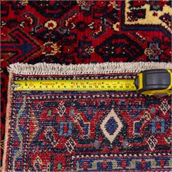 North West Persian Senneh hand-knotted rug, dark indigo field with a central bold stepped lozenge medallion of madder red and deep blue, enclosed within an ivory serrated contour forming a cruciform outline, medallion with repeating boteh and floral devices, field decorated with an all-over Herati pattern of rosettes enclosed by angular leaves principal border of madder red ground decorated with alternating floral heads, flanked by narrow guard stripes, with cotton fringe ends 