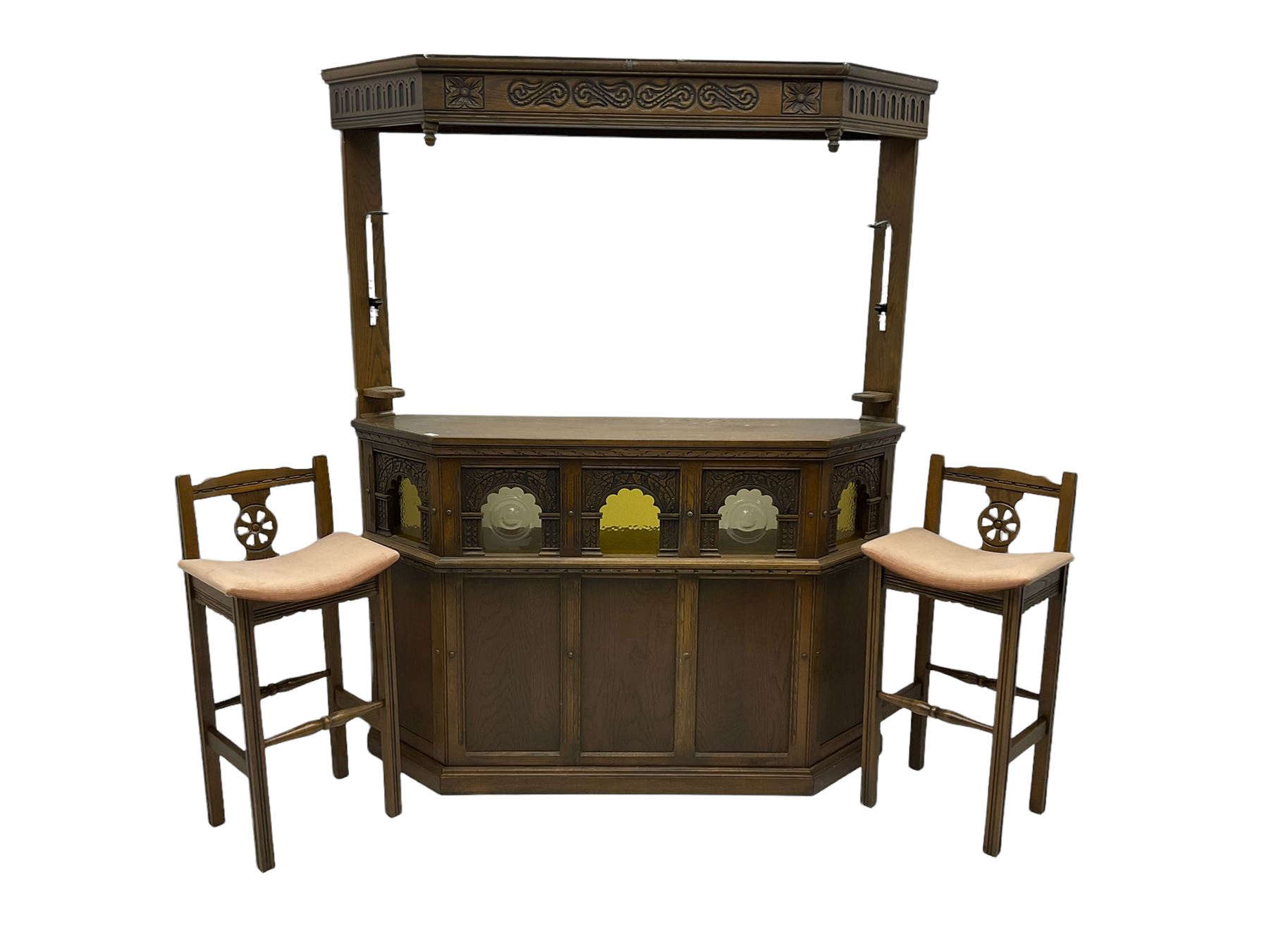 Old Charm - oak corner bar, the canopy frieze carved with scrolls, front decorated with arched apertures glazed with bullseye and mottled glass panes, skirted base, together with two bar stools