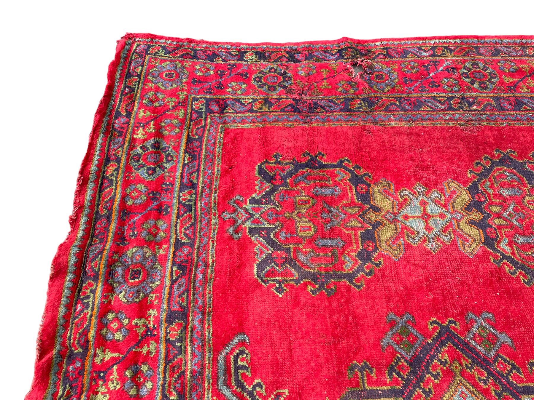 Early 20th century Western Anatolia Turkish Oushak crimson ground carpet, the field decorated with rows of Herati and Palmette medallions, the main border decorated with stylised flower head motifs within guard stripes