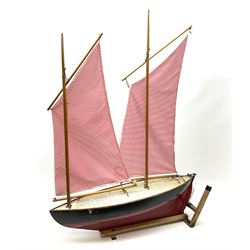 Mid-20th century pond yacht with red and black painted wooden hull, simulated planked deck bearing plaque for 'Hamleys 200-202 Regent Street London W1', two masts and sails and working rudder W65cm H89cm, on slatted pine stand