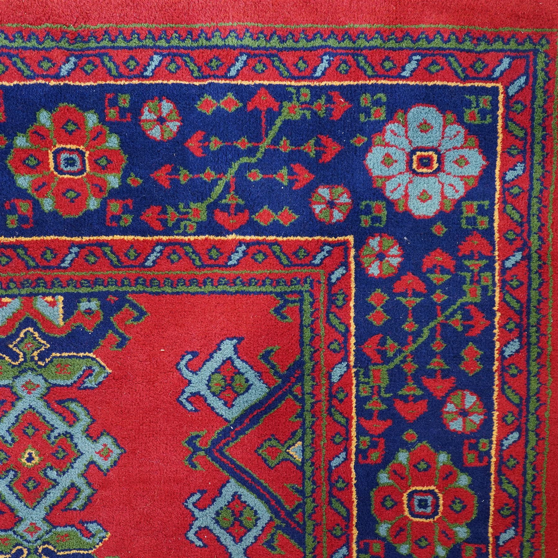 Indian Kayam rug, the rectangular field with repeating geometric medallions on a red ground, within a blue border of stylised floral motifs, with guard borders and fringe terminals