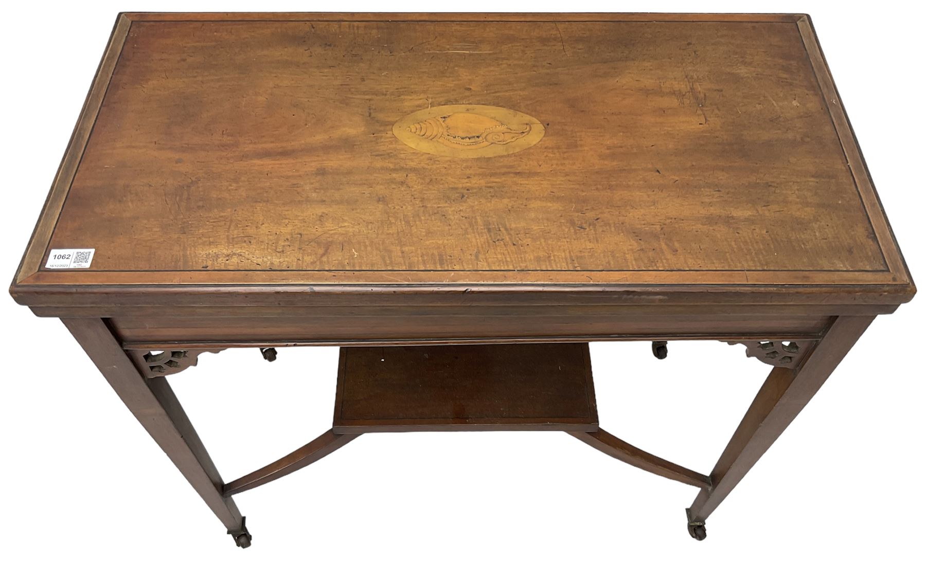Edwardian inlaid mahogany games table, the rectangular fold-over swivel top decorated with central shell motif inlay and ebony stringing, raised on tapering supports united by shaped X-stretcher and undertier